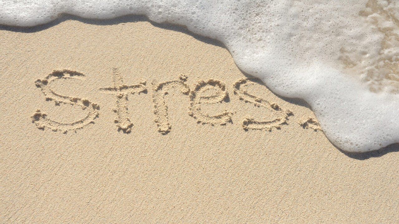 The word stress is written in the sand on the beach.