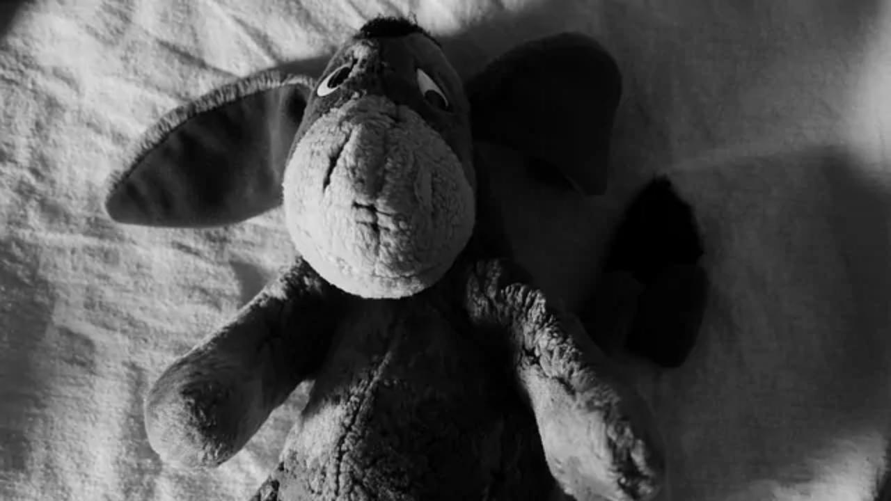 A stuffed donkey is laying on a bed in a black and white photo.