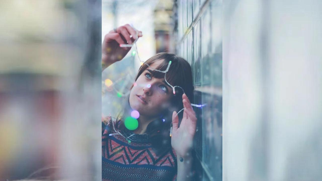 A woman wearing headphones and sunglasses is leaning against a wall.