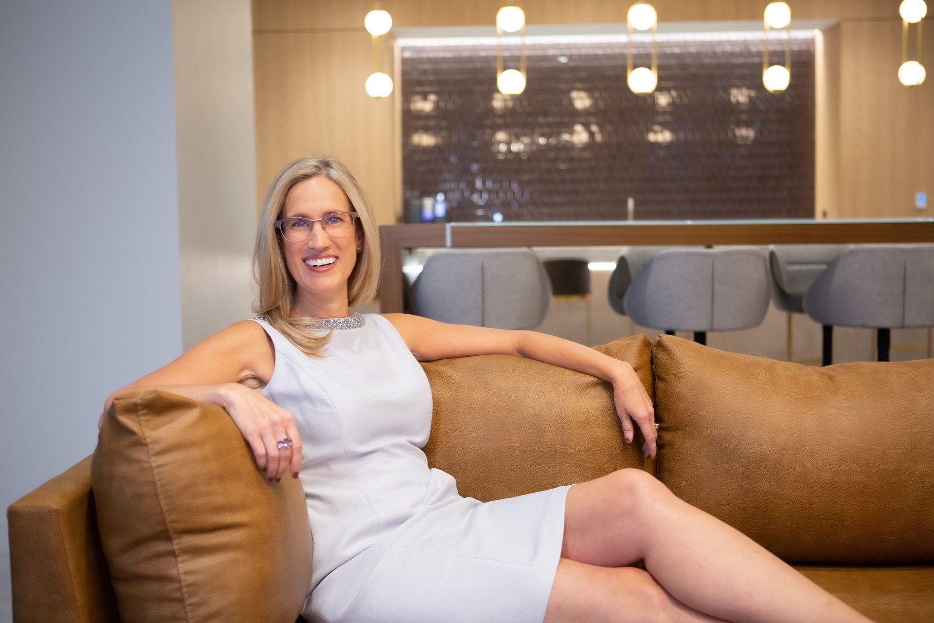 A woman in a white dress is sitting on a brown couch.