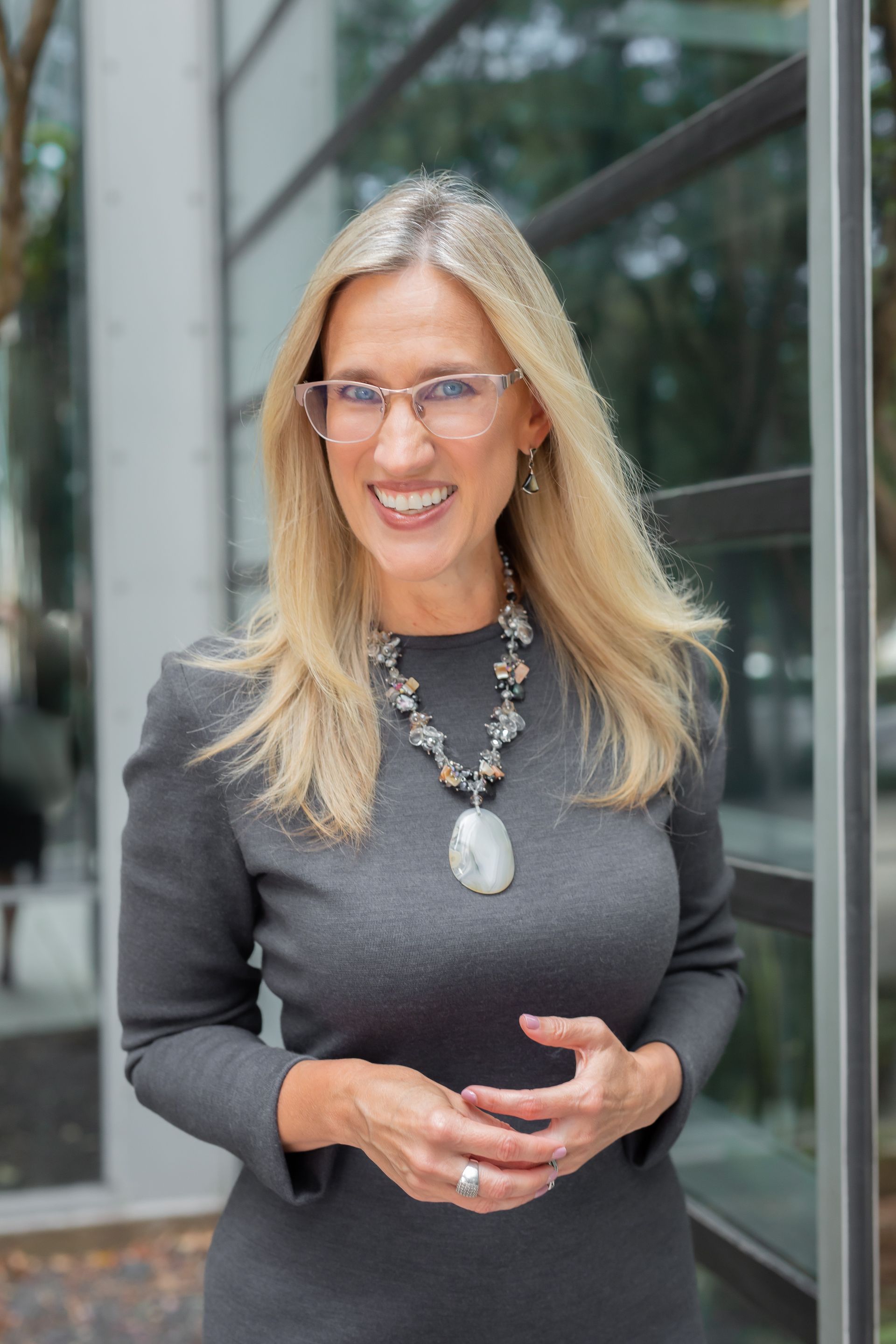 A woman wearing glasses and a necklace is standing in front of a building.