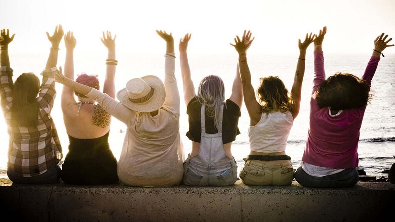 A group of women are sitting on a wall with their arms in the air.