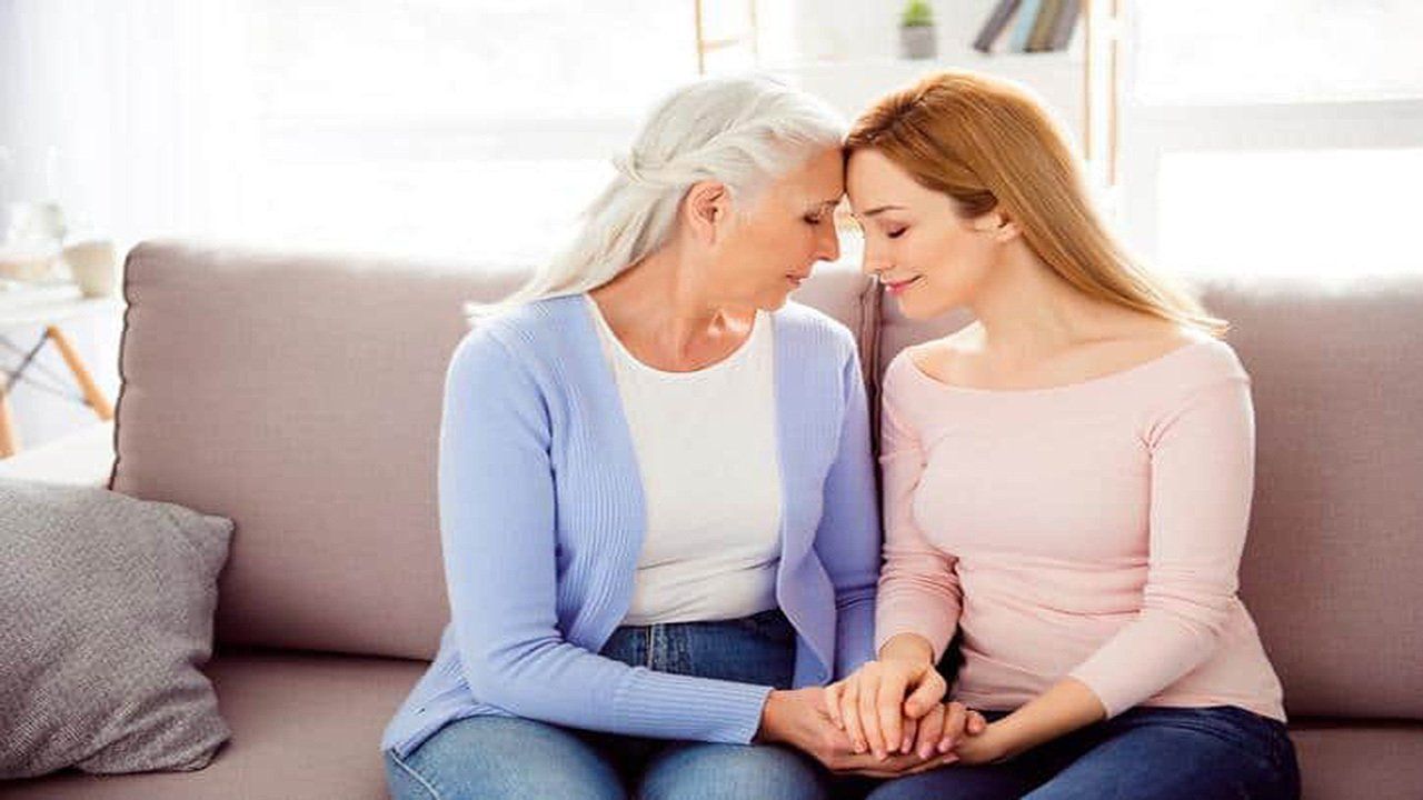 Two women are sitting on a couch holding hands and looking at each other.