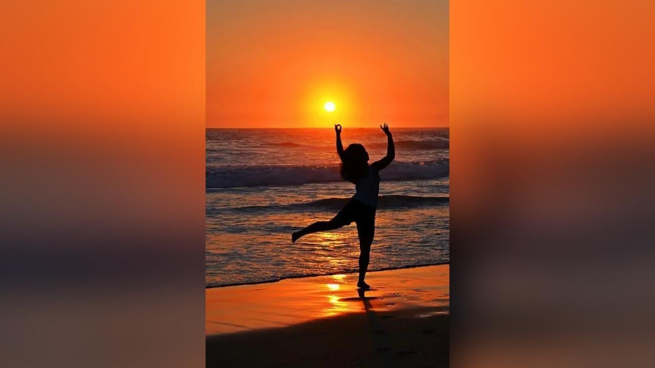 A woman is dancing on the beach at sunset.