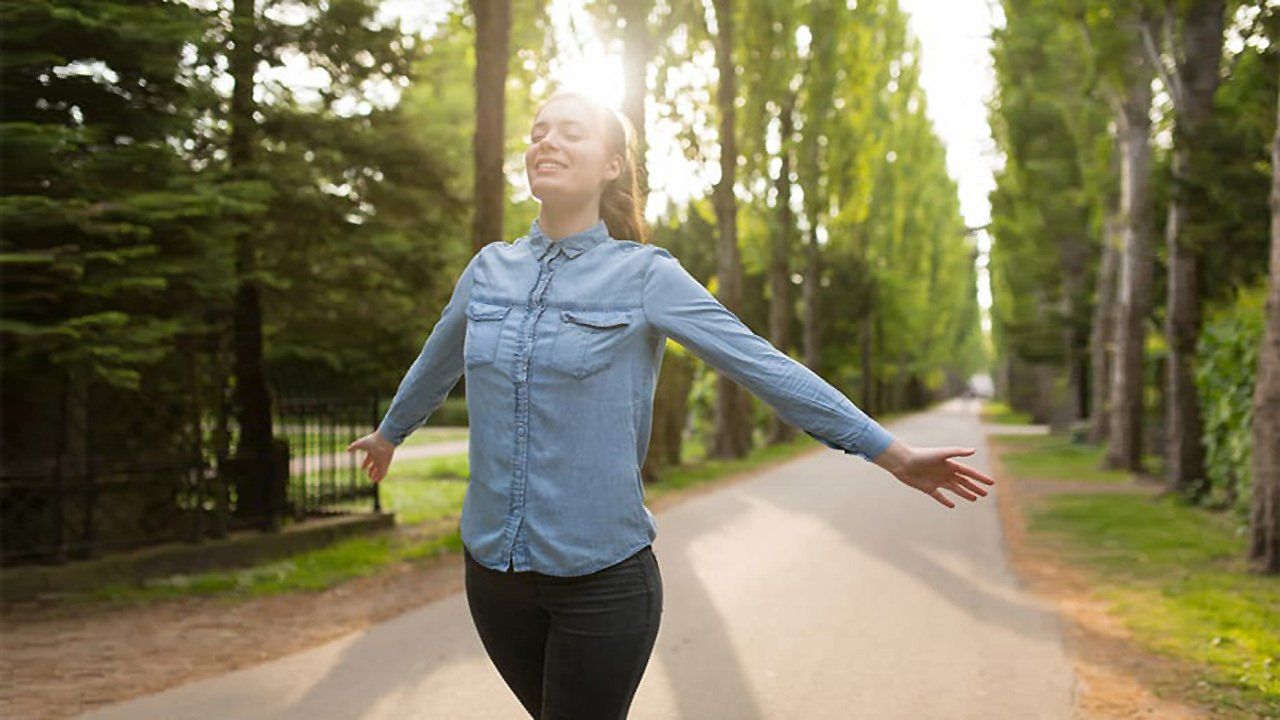 A woman is walking down a road with her arms outstretched.