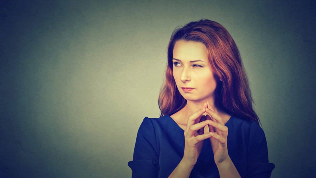 A woman with red hair is sitting with her hands folded in front of her face.