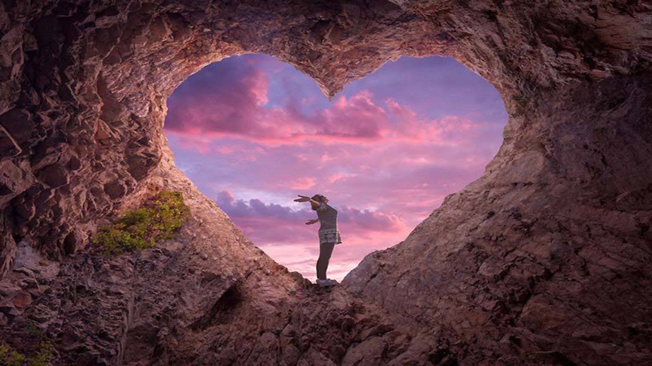 A man is standing in a cave with a heart shaped hole in the rocks.