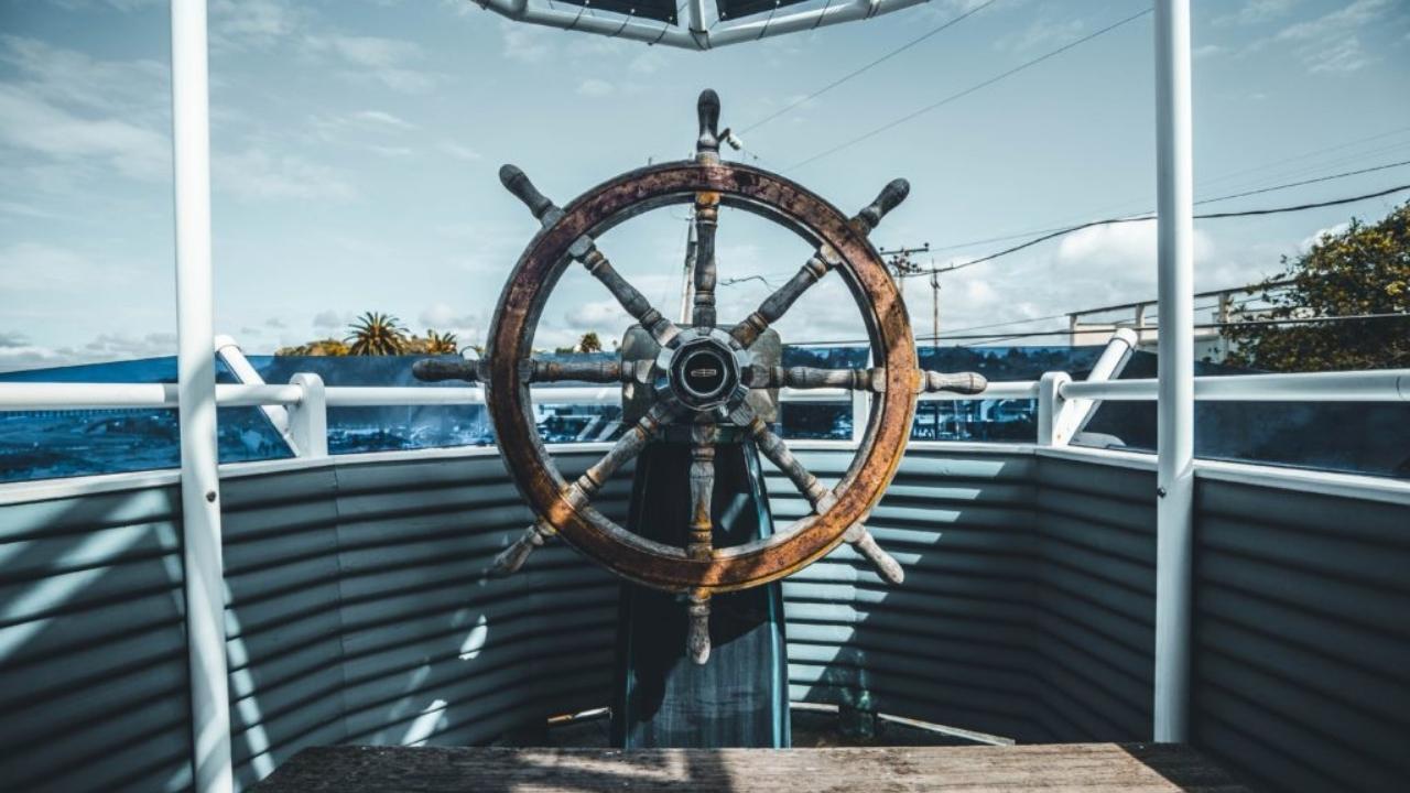 A wooden steering wheel is on the deck of a boat.