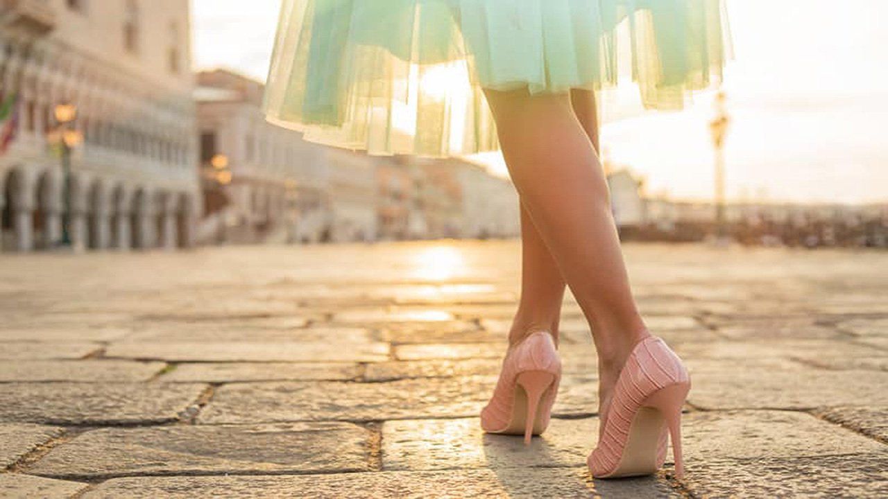A woman in a green skirt and pink high heels is walking down a cobblestone street.