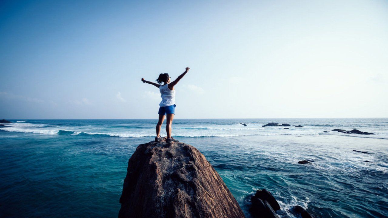A woman is standing on top of a rock overlooking the ocean.