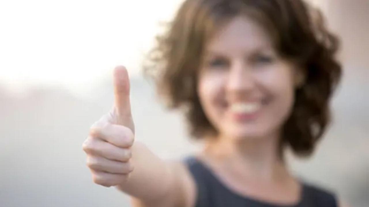 A woman is smiling and giving a thumbs up sign.