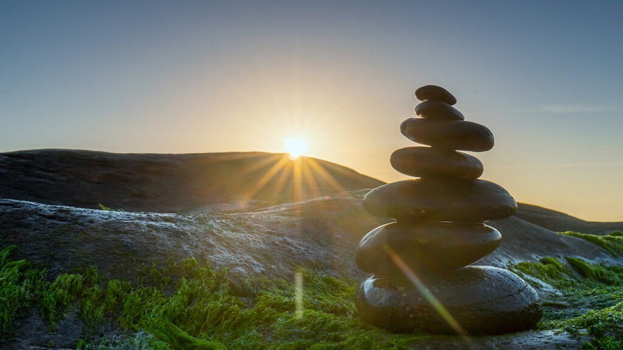 A stack of rocks sitting on top of each other on a hill with the sun shining through the rocks.