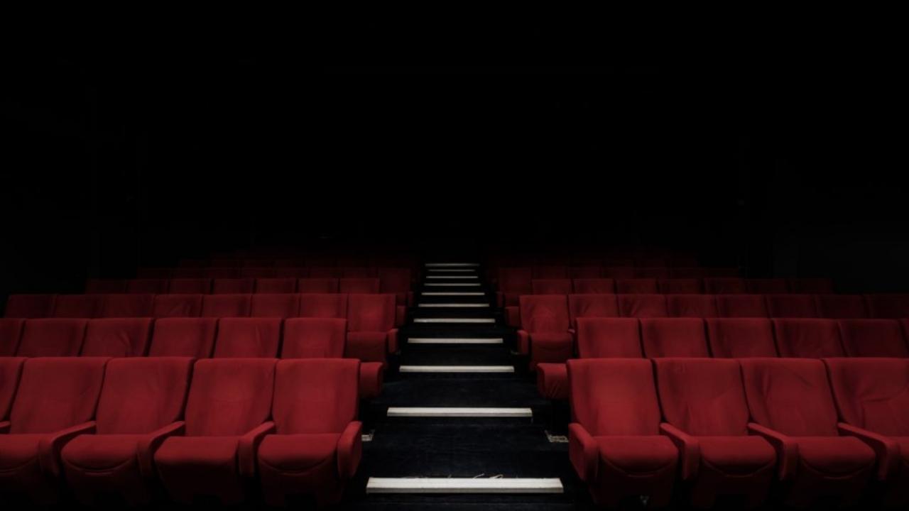 A row of red seats in an empty theater with stairs leading up to them.