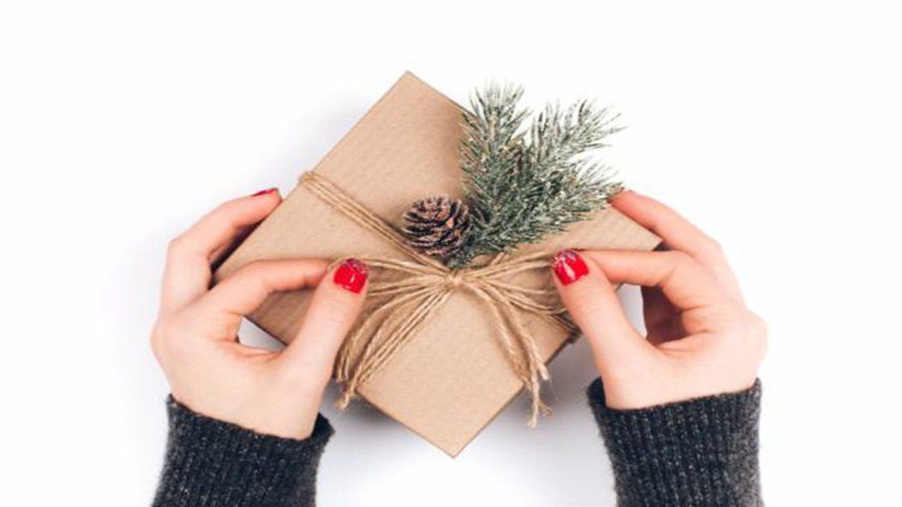 A woman is holding a christmas present wrapped in brown paper.
