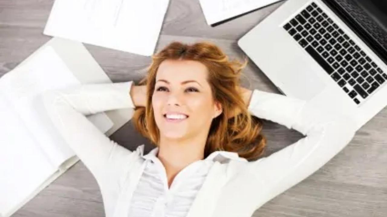A woman is laying on the floor with her hands behind her head surrounded by laptops and papers.