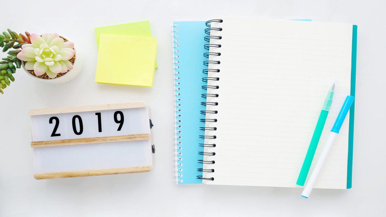 A notebook , pen , sticky notes , and a sign that says `` 2019 '' on a table.