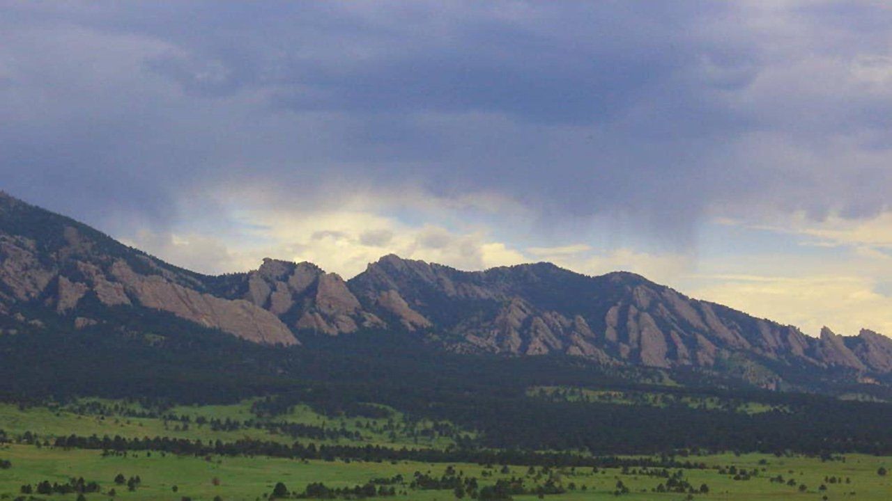 A mountain range with a field in the foreground and a cloudy sky in the background.