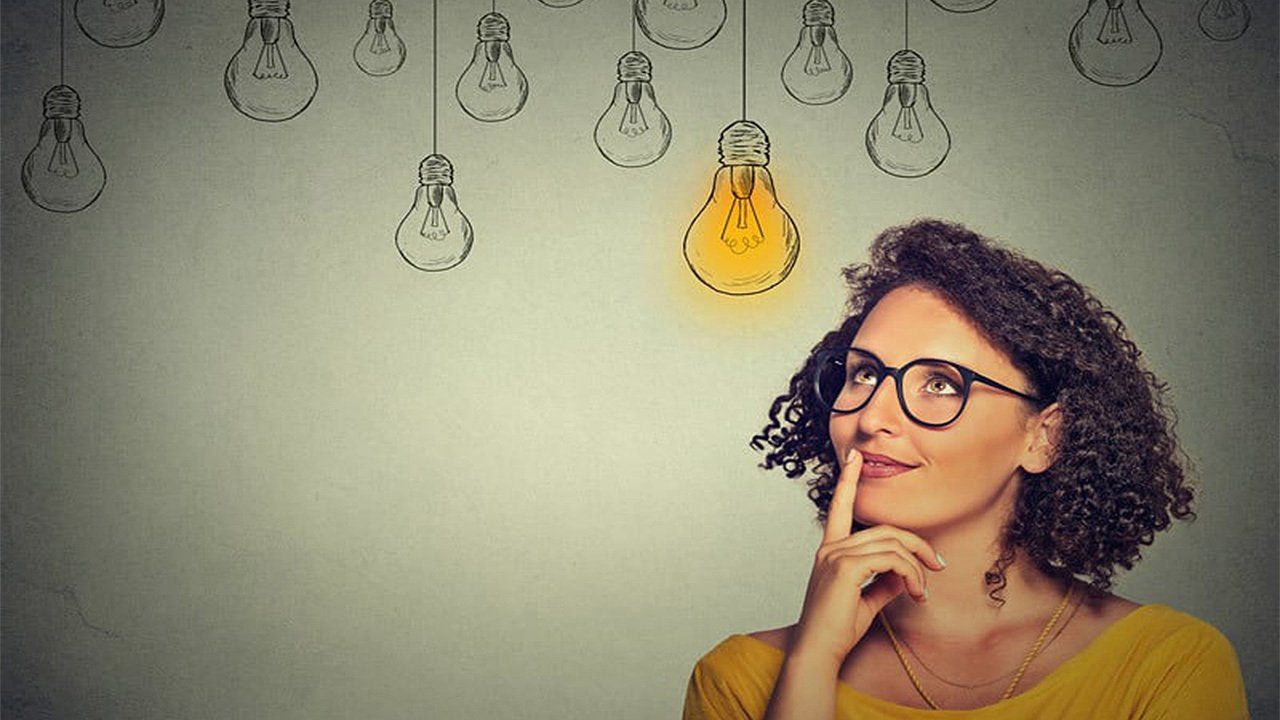 A woman wearing glasses is looking up at a drawing of light bulbs on a wall.