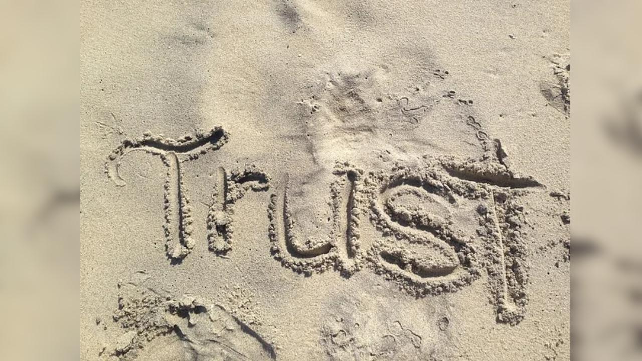 The word trust is written in the sand on a piece of paper.