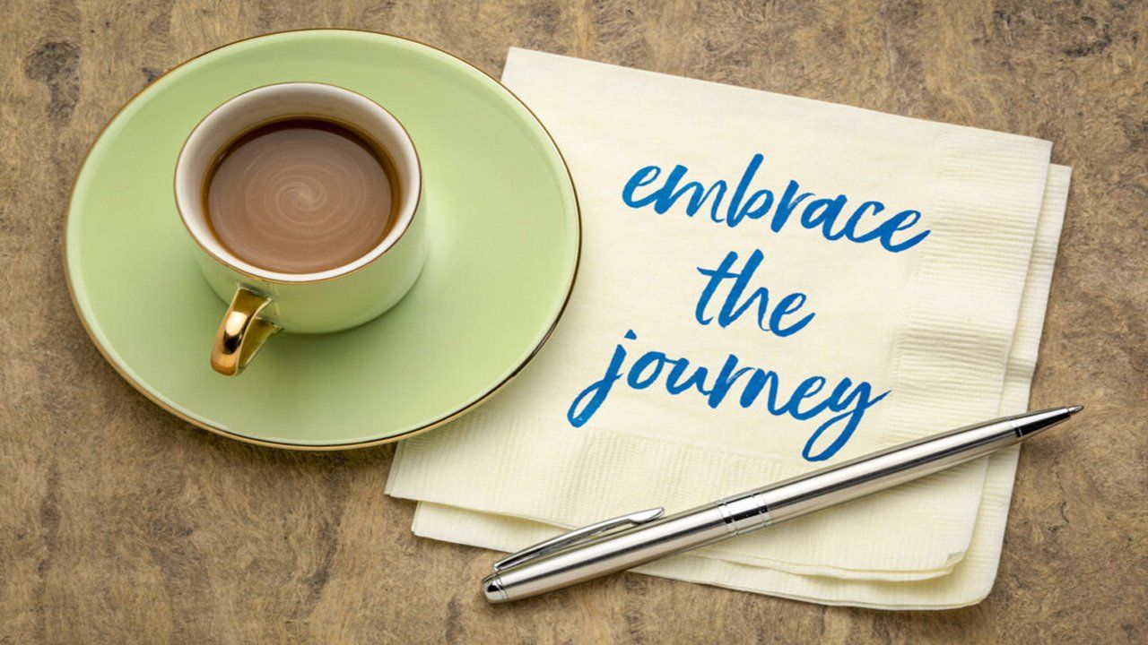A napkin with the words embrace the journey written on it next to a cup of coffee.