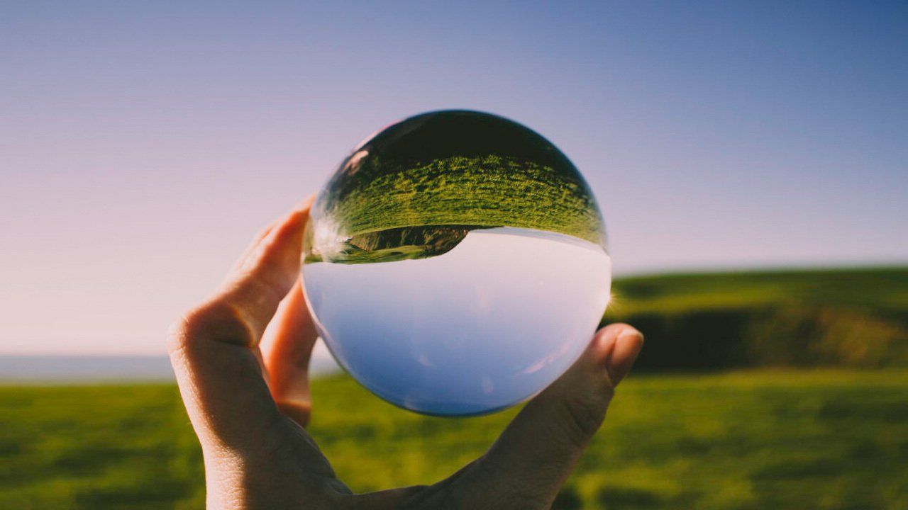 A person is holding a glass ball with a reflection of a field in it.