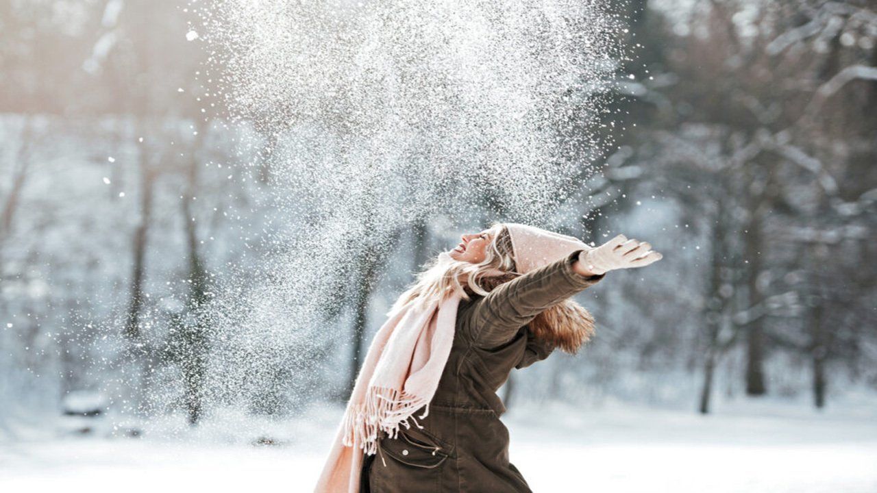 A woman is throwing snow in the air while wearing a scarf.