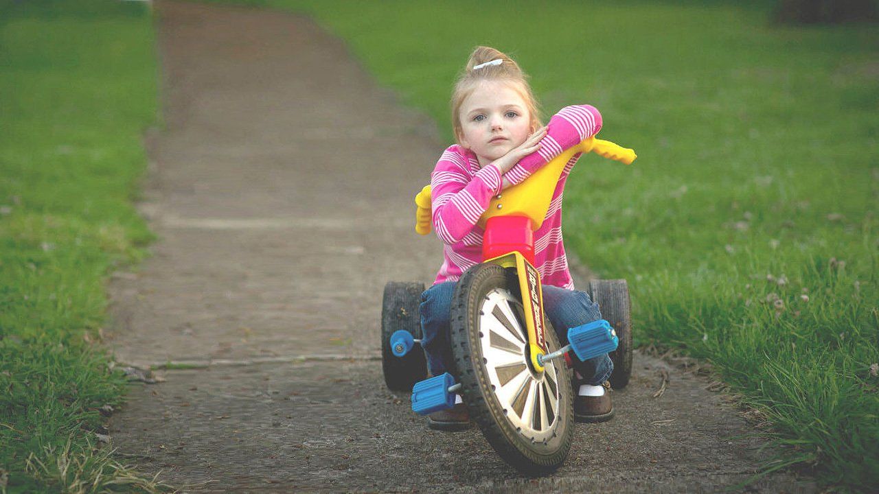 A little girl is riding a tricycle down a sidewalk.