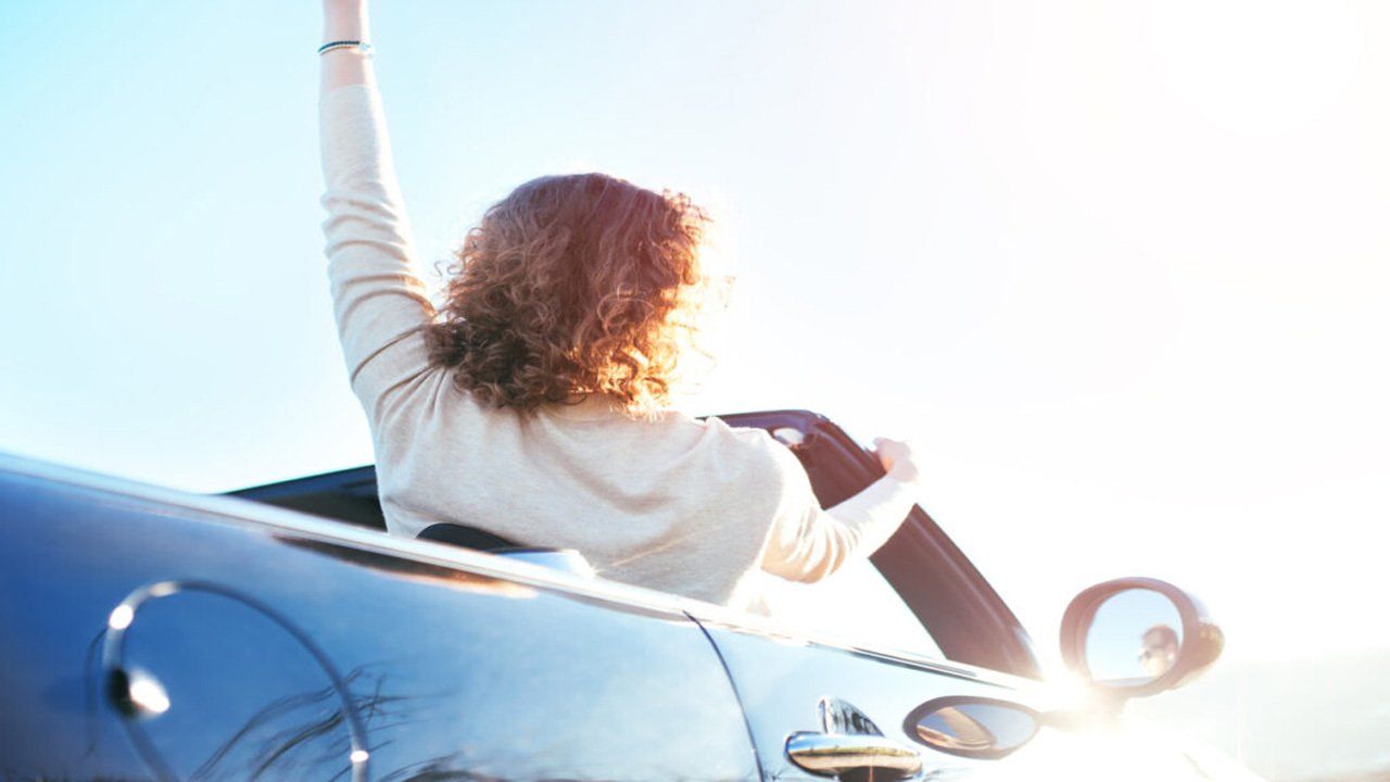 A woman is sitting in the back of a convertible car with her arms in the air.