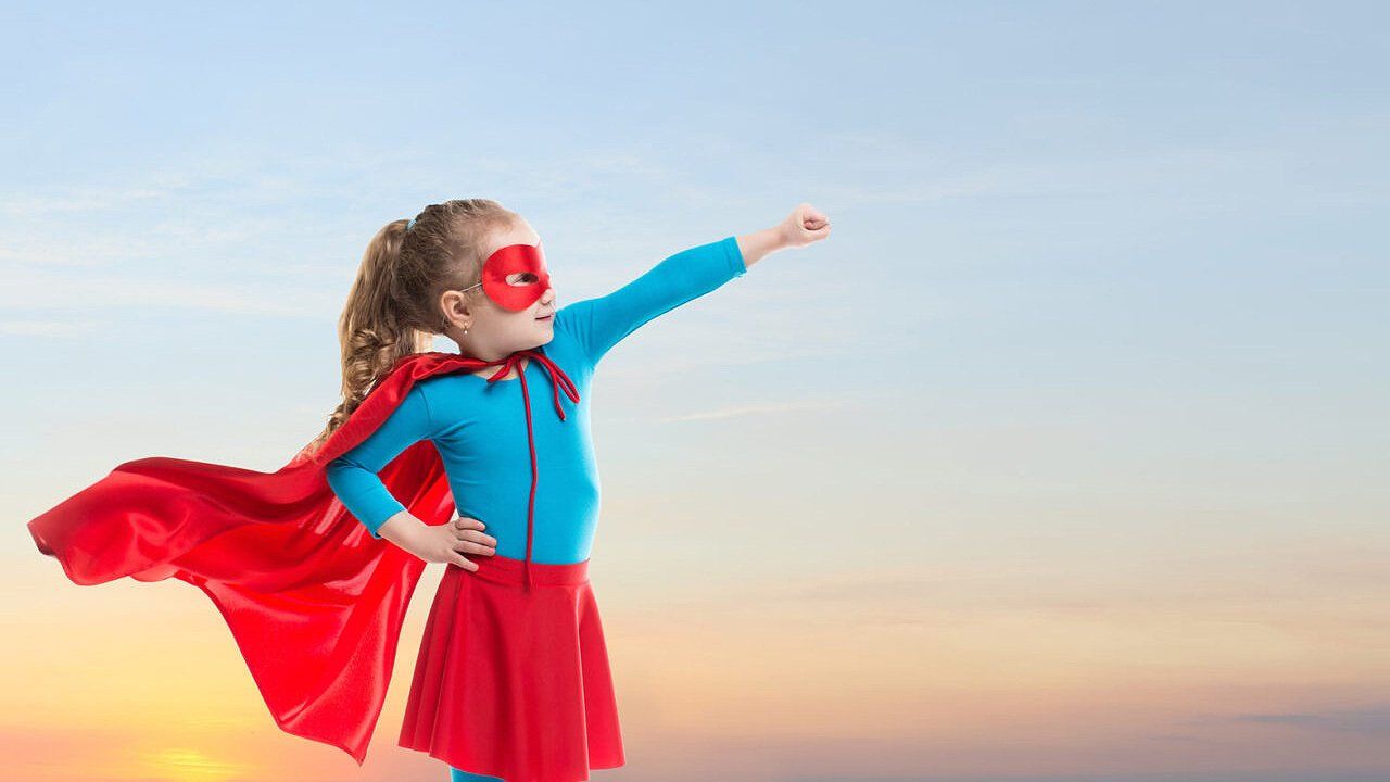 A little girl is dressed as a superhero with a red cape and mask.