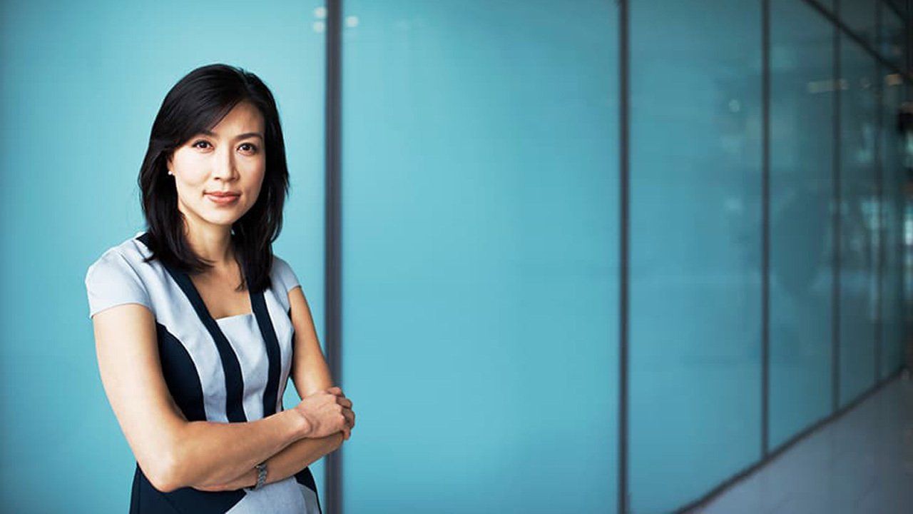 A woman is standing in front of a blue wall with her arms crossed.