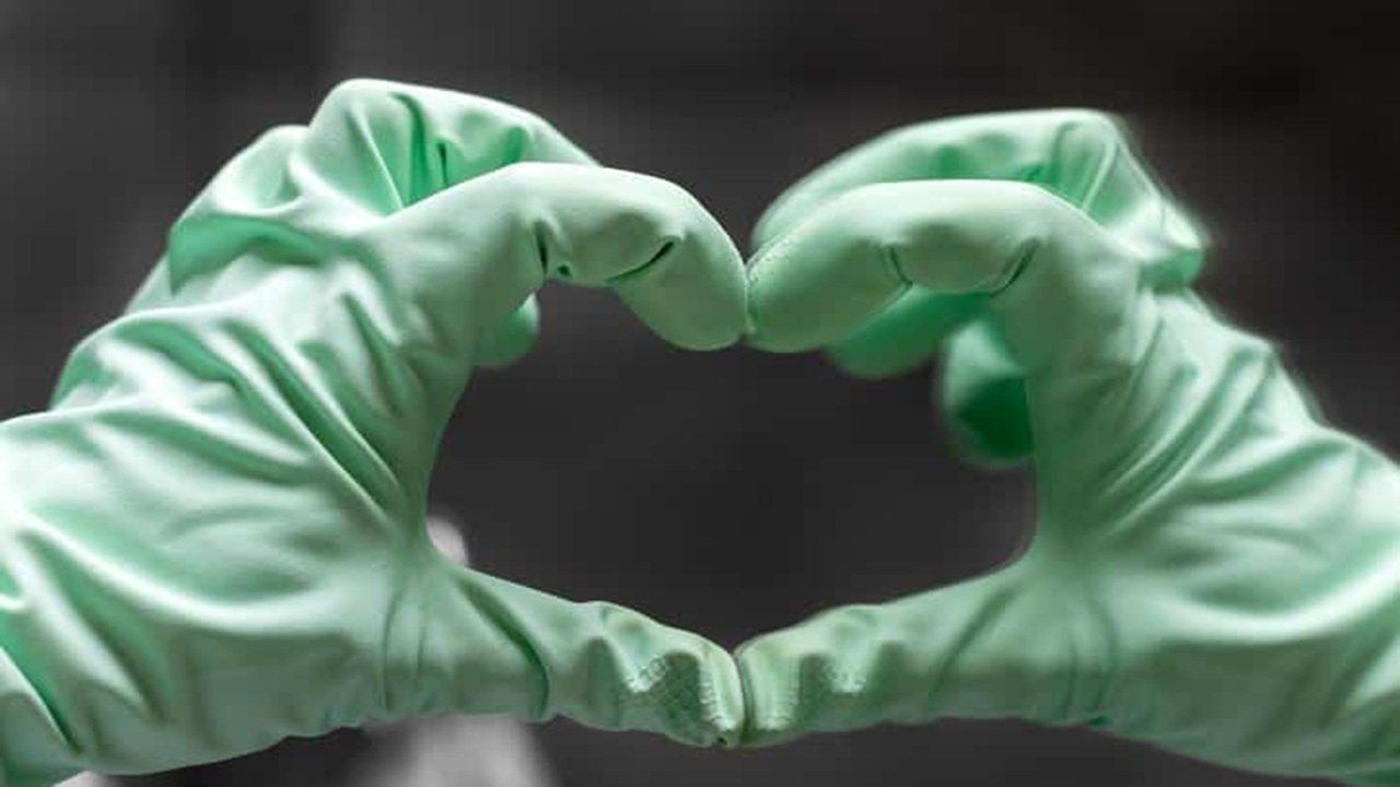 A person wearing green gloves is making a heart shape with their hands.