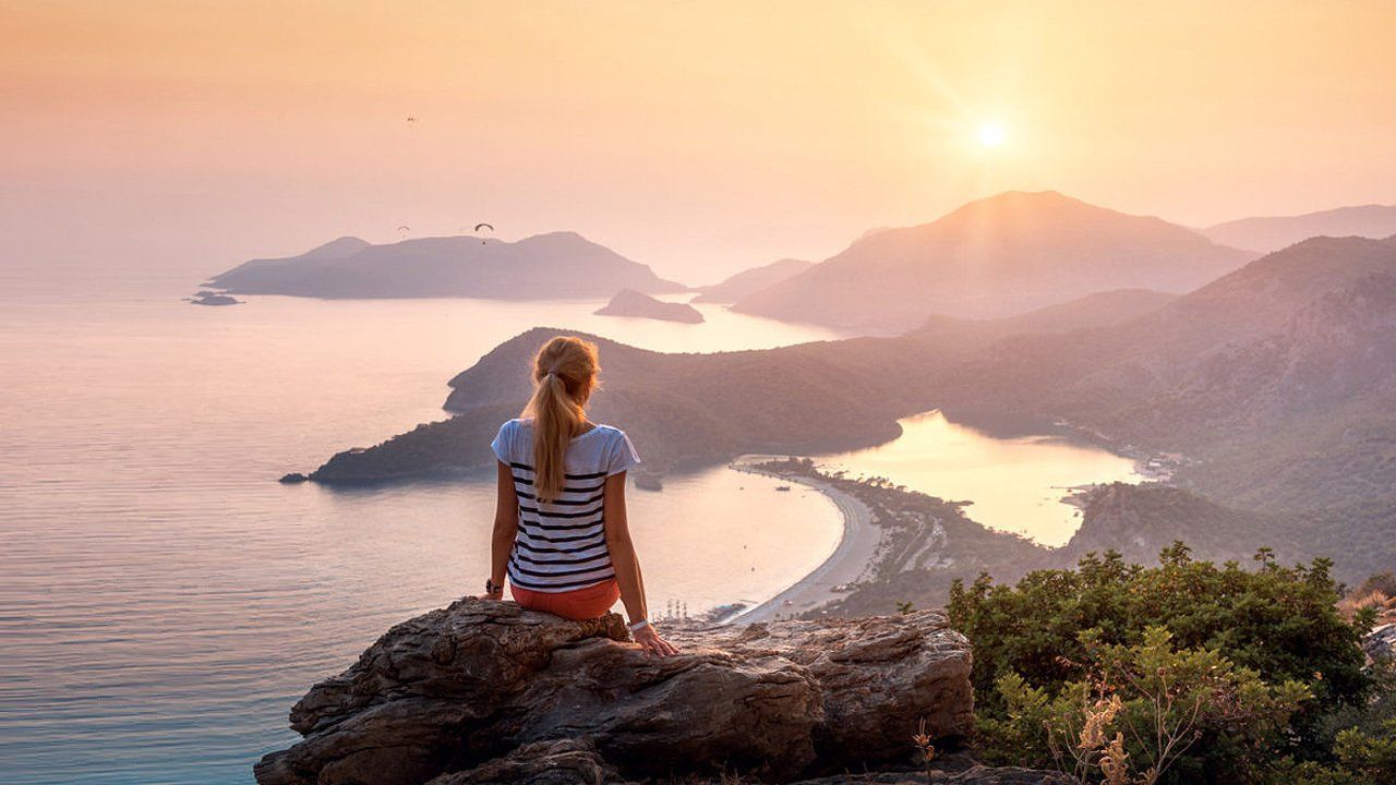A woman is sitting on top of a mountain overlooking the ocean.