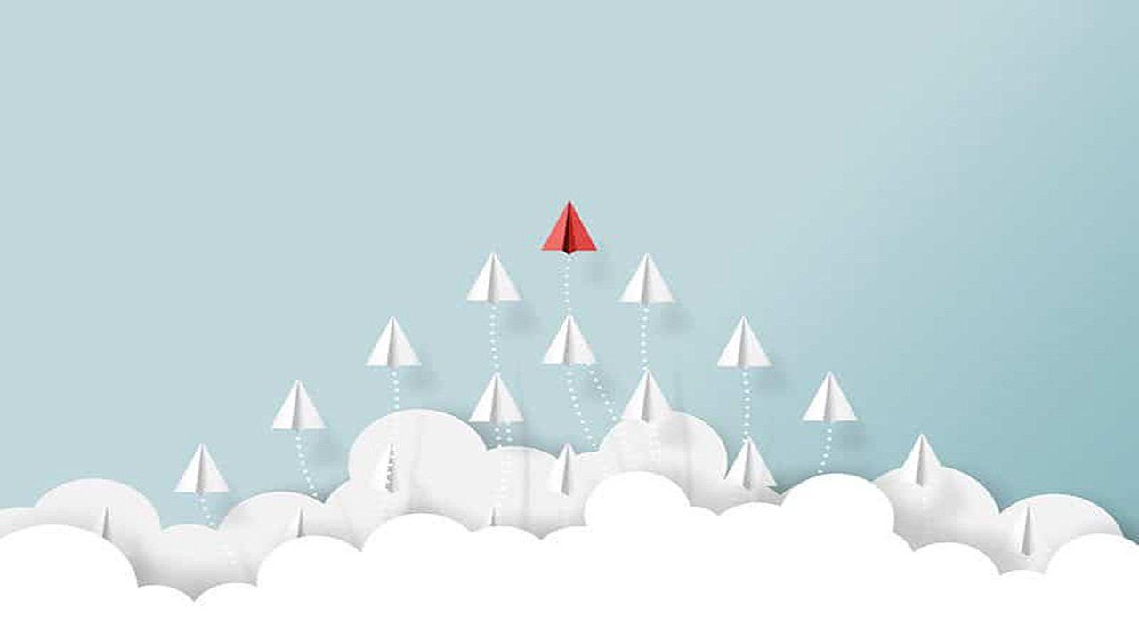A red paper airplane is flying in the sky above a group of white paper airplanes.