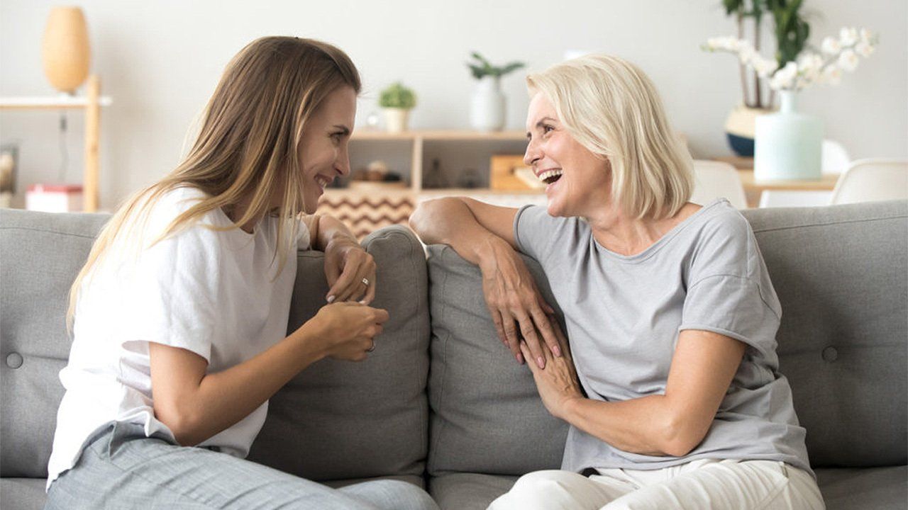 Two women are sitting on a couch talking to each other.