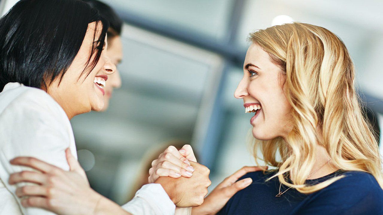 Two women are holding hands and smiling at each other.