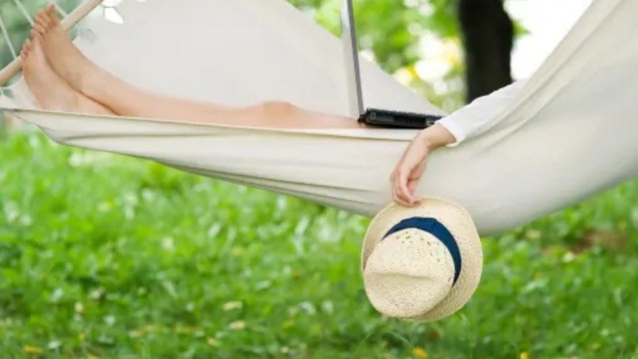 A person is laying in a hammock with a laptop and a hat