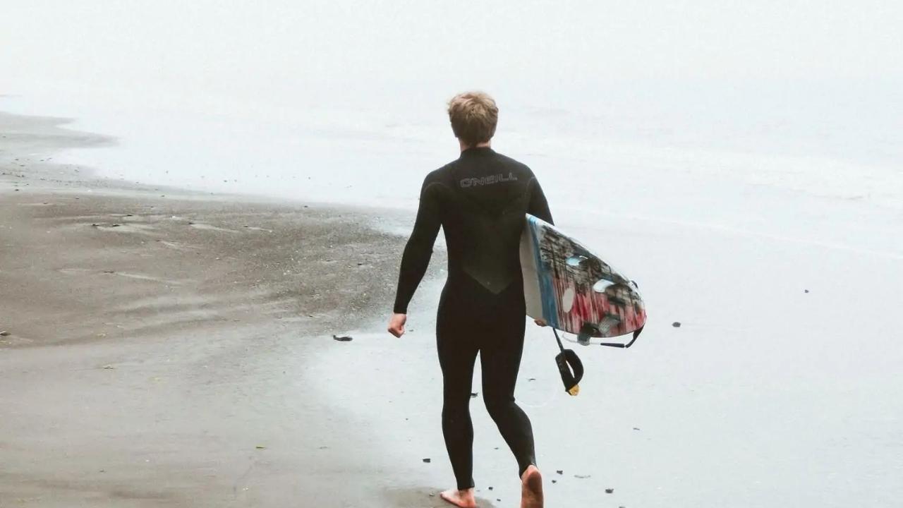 A man in a wetsuit is walking on the beach with a surfboard.