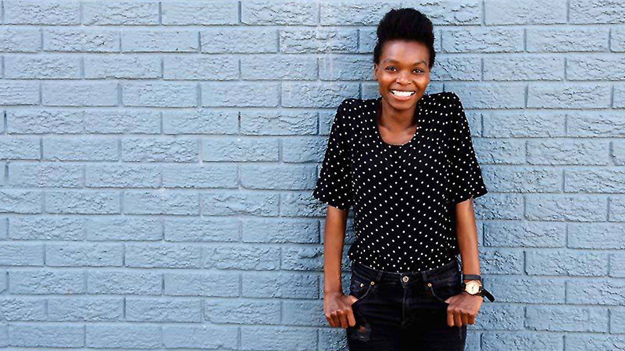 A woman is standing in front of a blue brick wall.