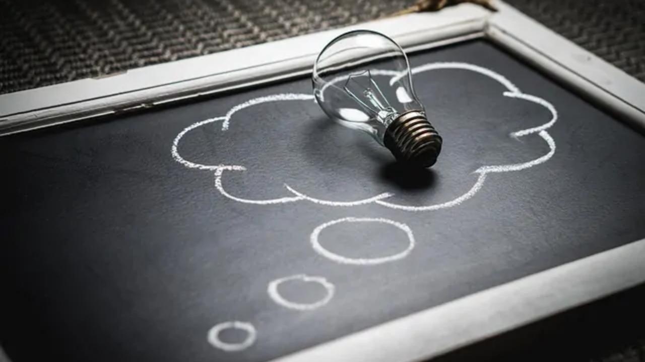 A light bulb is sitting on top of a blackboard with a thought bubble drawn on it.