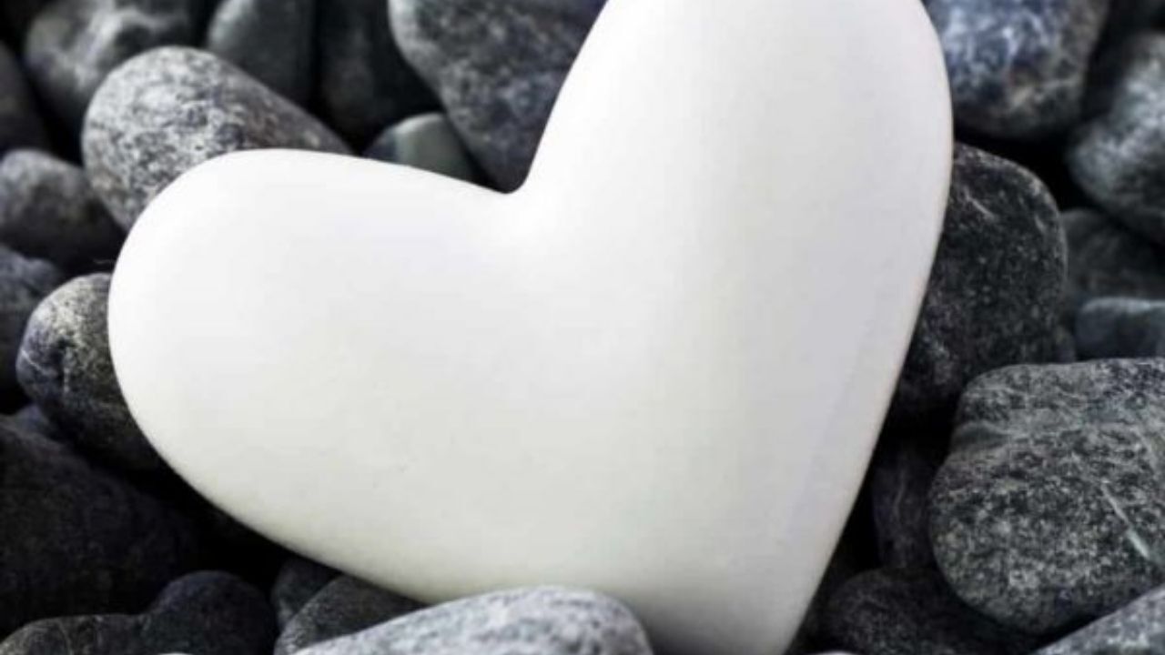A white heart is sitting on top of a pile of rocks.