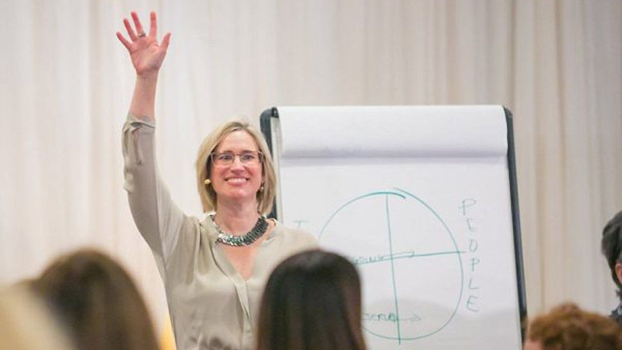 A woman is giving a presentation to a group of people and raising her hand in the air.
