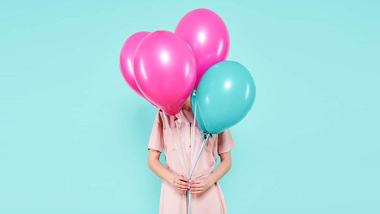 A woman in a pink dress is holding balloons in front of her face.