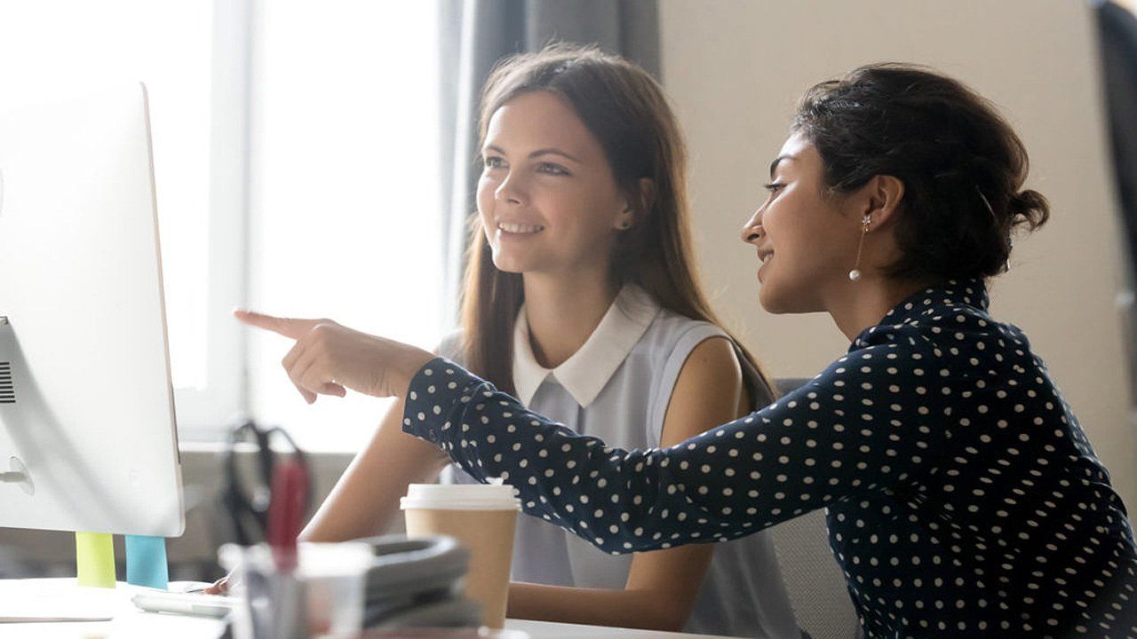 Two women are sitting at a desk looking at a computer screen.