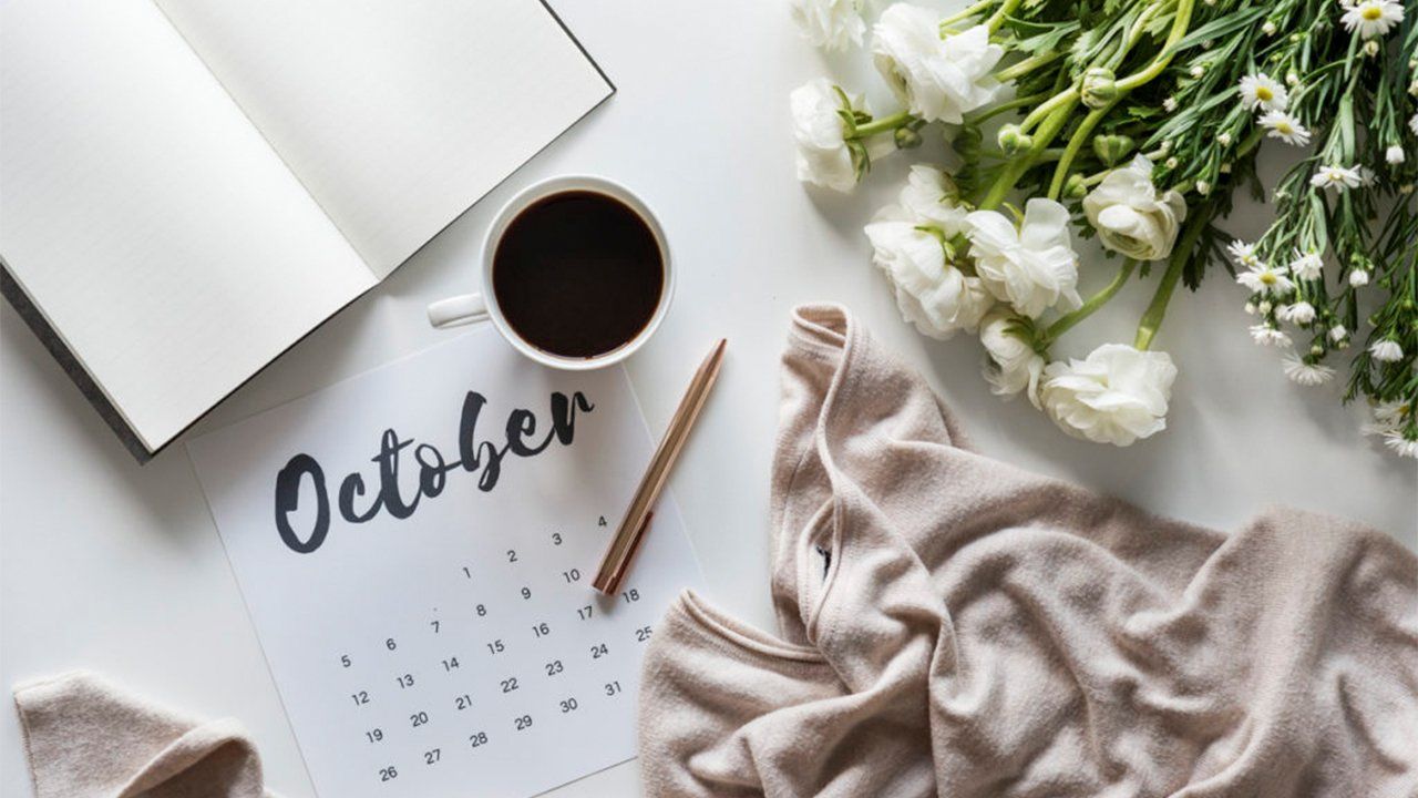 A calendar , a cup of coffee , a notebook , and flowers on a table.