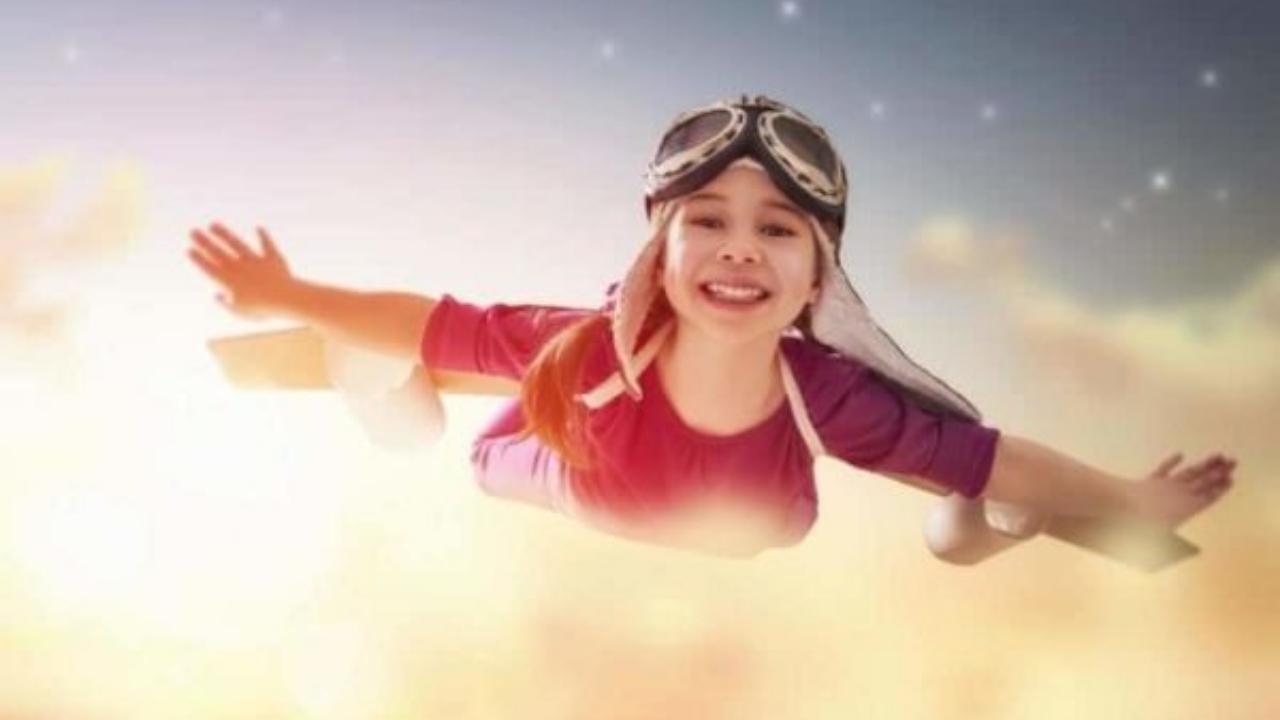A little girl is flying through the air wearing a pilot 's hat and goggles.