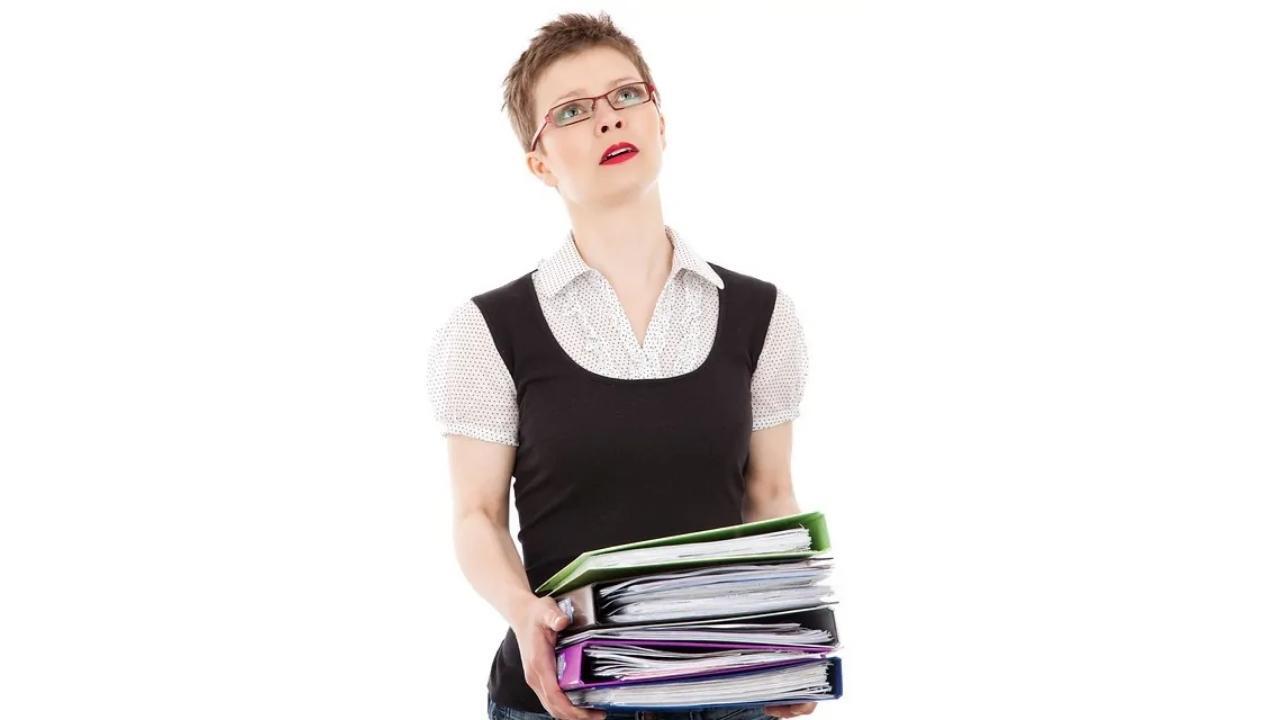 A woman is holding a stack of binders in her hands.