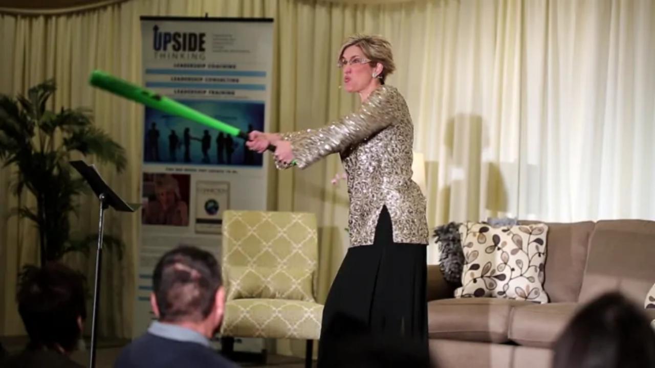 A woman is holding a green bat in front of a sign that says ' upside ' on it.