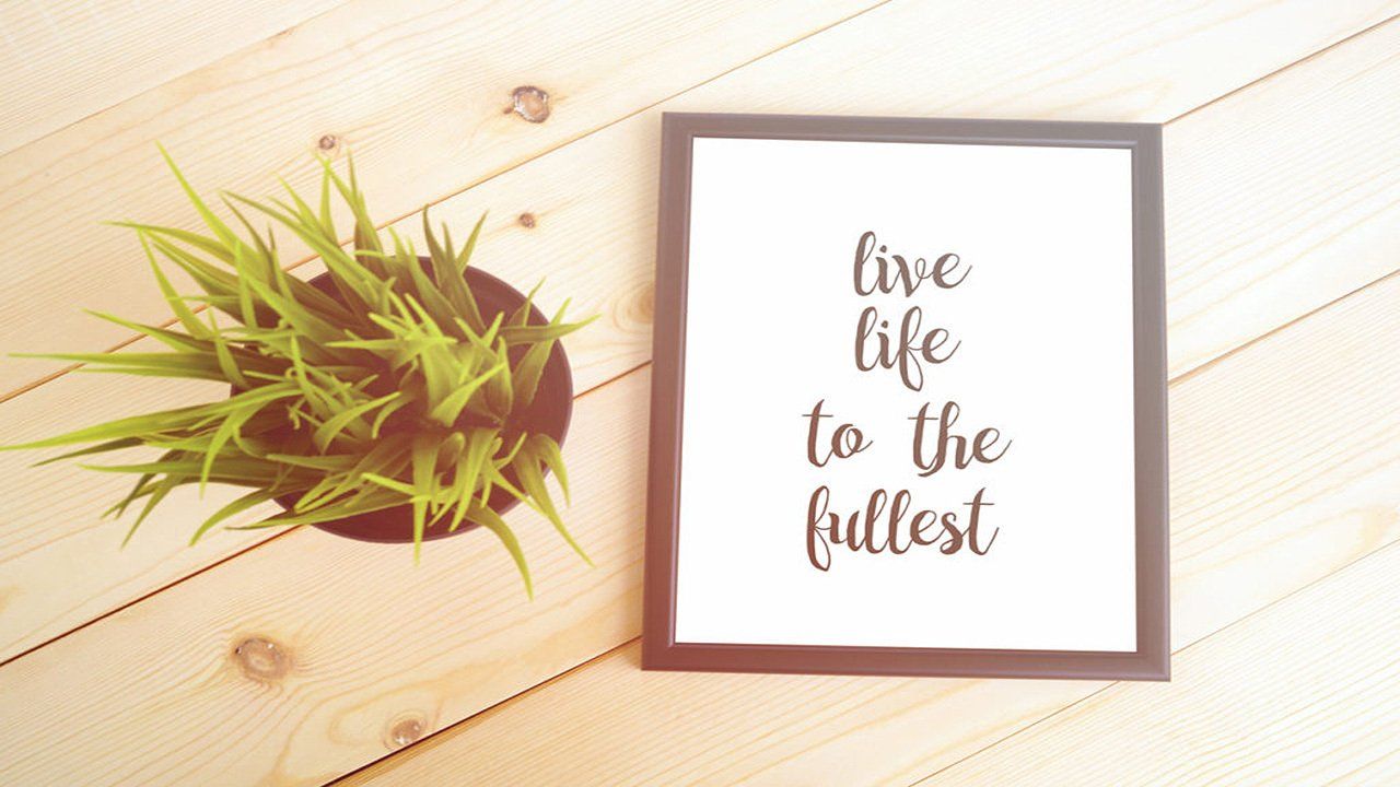 A picture frame with the words `` live life to the fullest '' next to a potted plant on a wooden table.