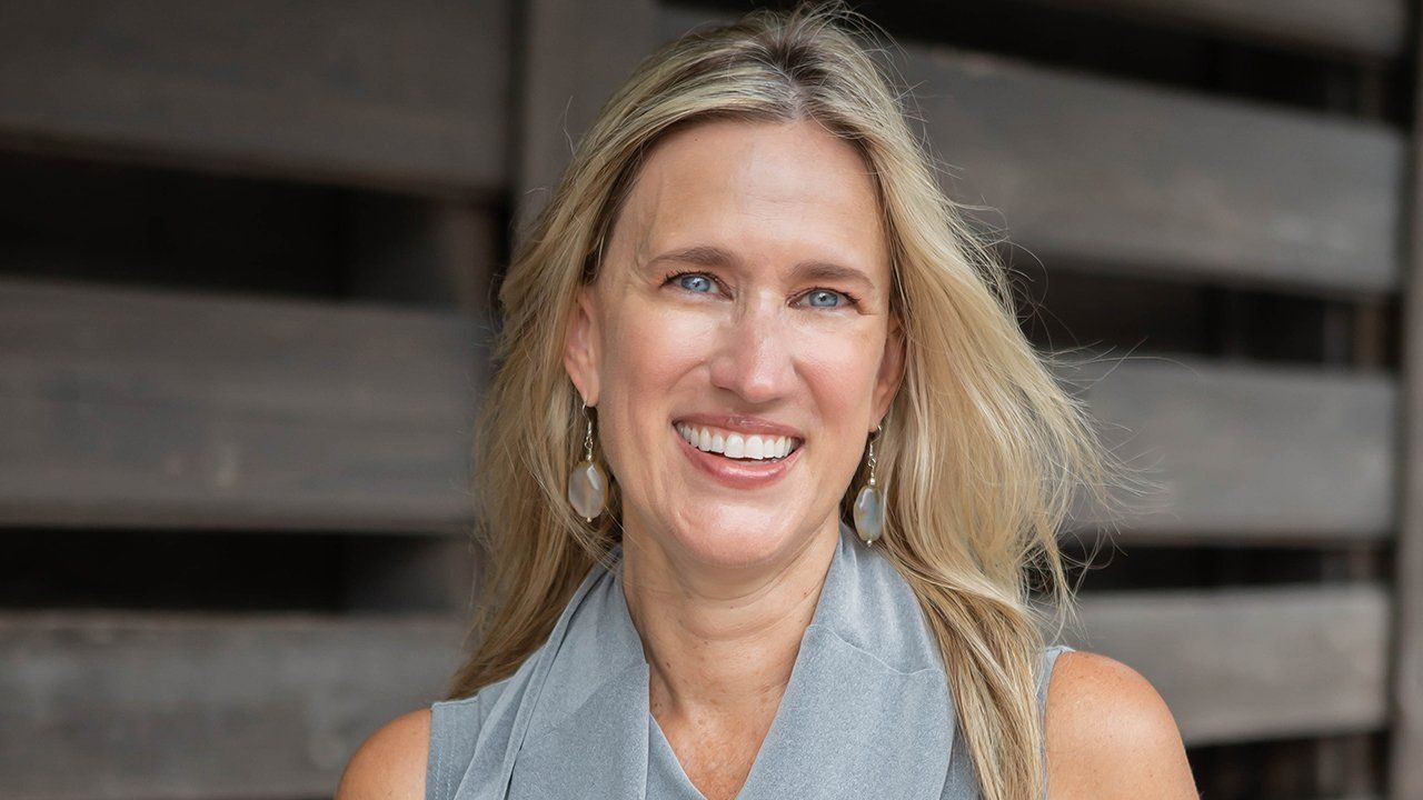 A woman is smiling for the camera while standing in front of a wooden wall.