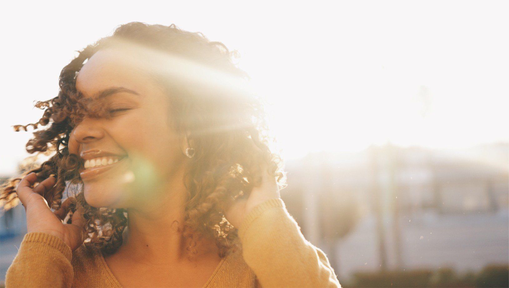 A woman is smiling while holding her hair in front of the sun.